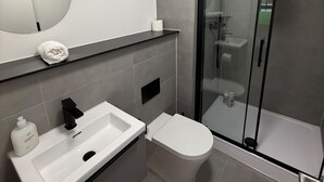 Ein modernes Badezimmer mit einer gläsernen Duschkabine, einem weißen Waschbecken und einer Toilette.