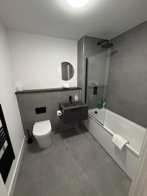 A modern bathroom with a toilet, sink, mirror, and shower.