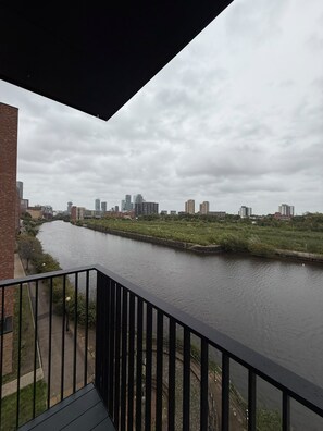 A river with a bridge, a city skyline in the background, and a balcony with a railing.
