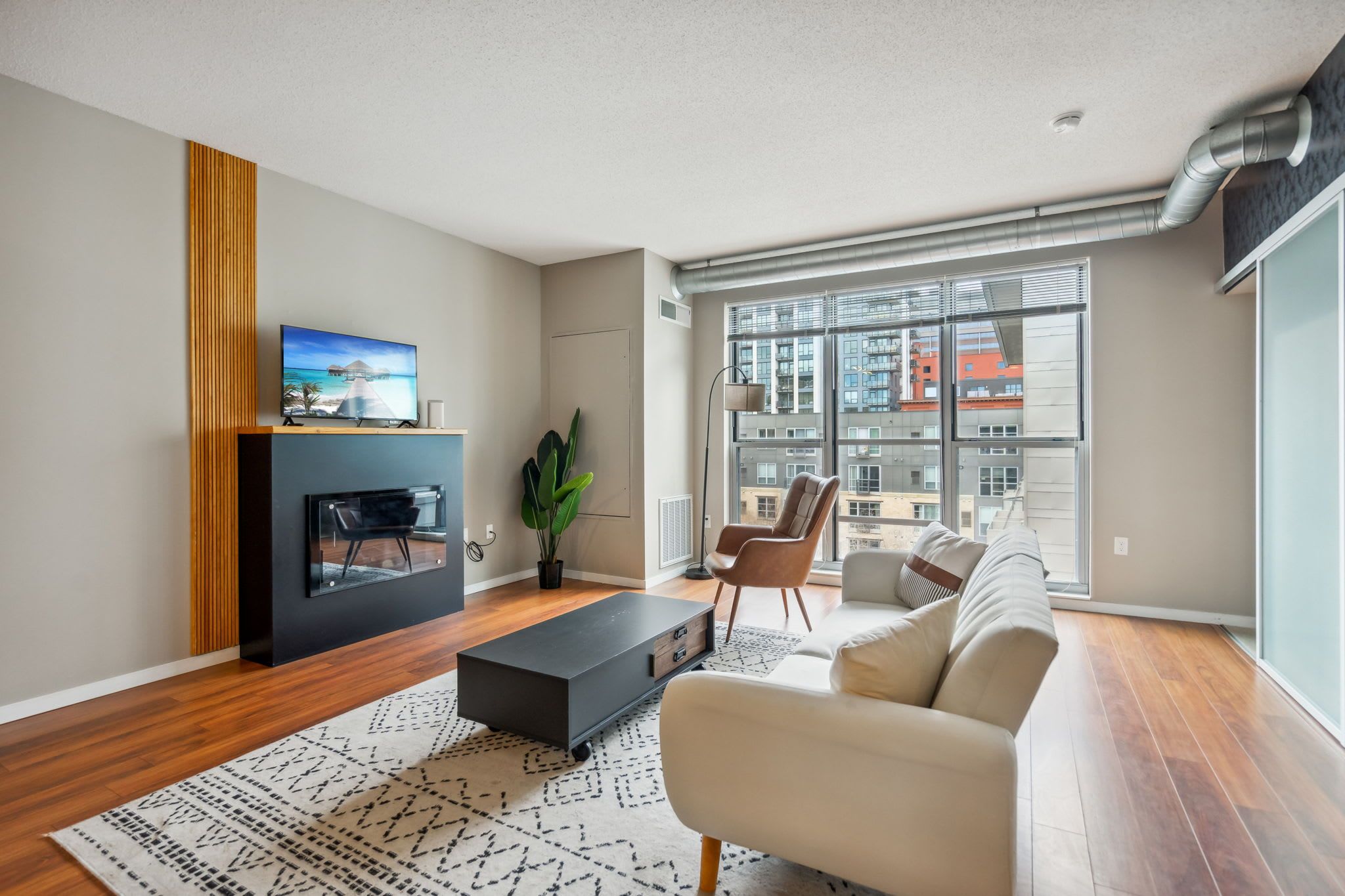 Ein modernes Wohnzimmer mit Kamin, einer Couch, einem Couchtisch und einem großen Fenster mit Blick auf die Stadt.