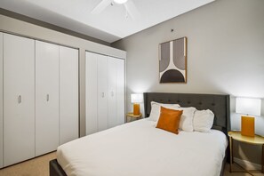 Ein Hotelzimmer mit einem großen Bett, zwei Nachttischen mit Lampen, einem grauen Kopfteil und einem Kleiderschrank mit Schiebetüren.