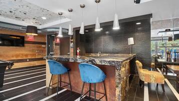 A modern bar area with a marble countertop, two blue bar stools, and hanging pendant lights.