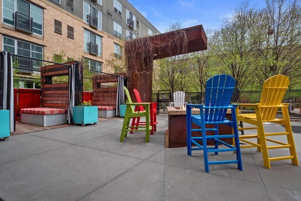 An outdoor seating area with colorful Adirondack chairs, a fire pit, and a wooden pergola.