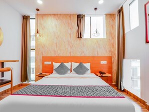 A hotel room with a large bed, a wooden headboard, two bedside tables, a desk, and a chair. - Townhouse Casa Grand (Hyderabad)