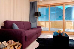 Ein Wohnzimmer mit einem roten Sofa, einer Lampe, Holzboden und einem Fenster mit Bergblick.