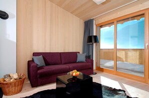 Ein modernes Wohnzimmer mit Holzbalkendecke, einem roten Sofa mit grauen Kissen, einem schwarzen Couchtisch mit Obst und einer Glastür zu einem Balkon.