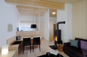 Ein modernes Wohnzimmer mit Sofa, einem Essbereich mit Tisch und Stühlen sowie einer Küche mit Holzausbau und einem schwarzen Herd.