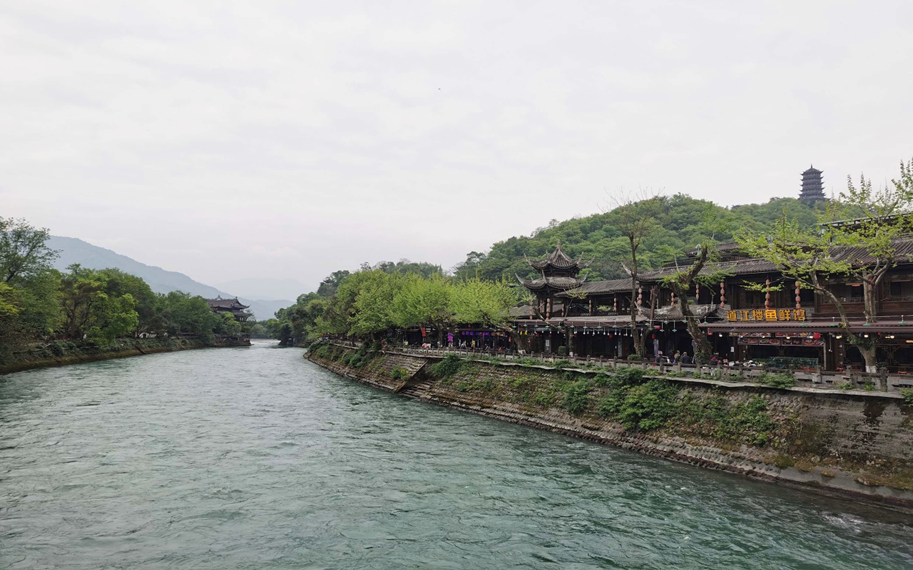 Vista a la orilla del río con arquitectura tradicional, un puente y una pagoda.