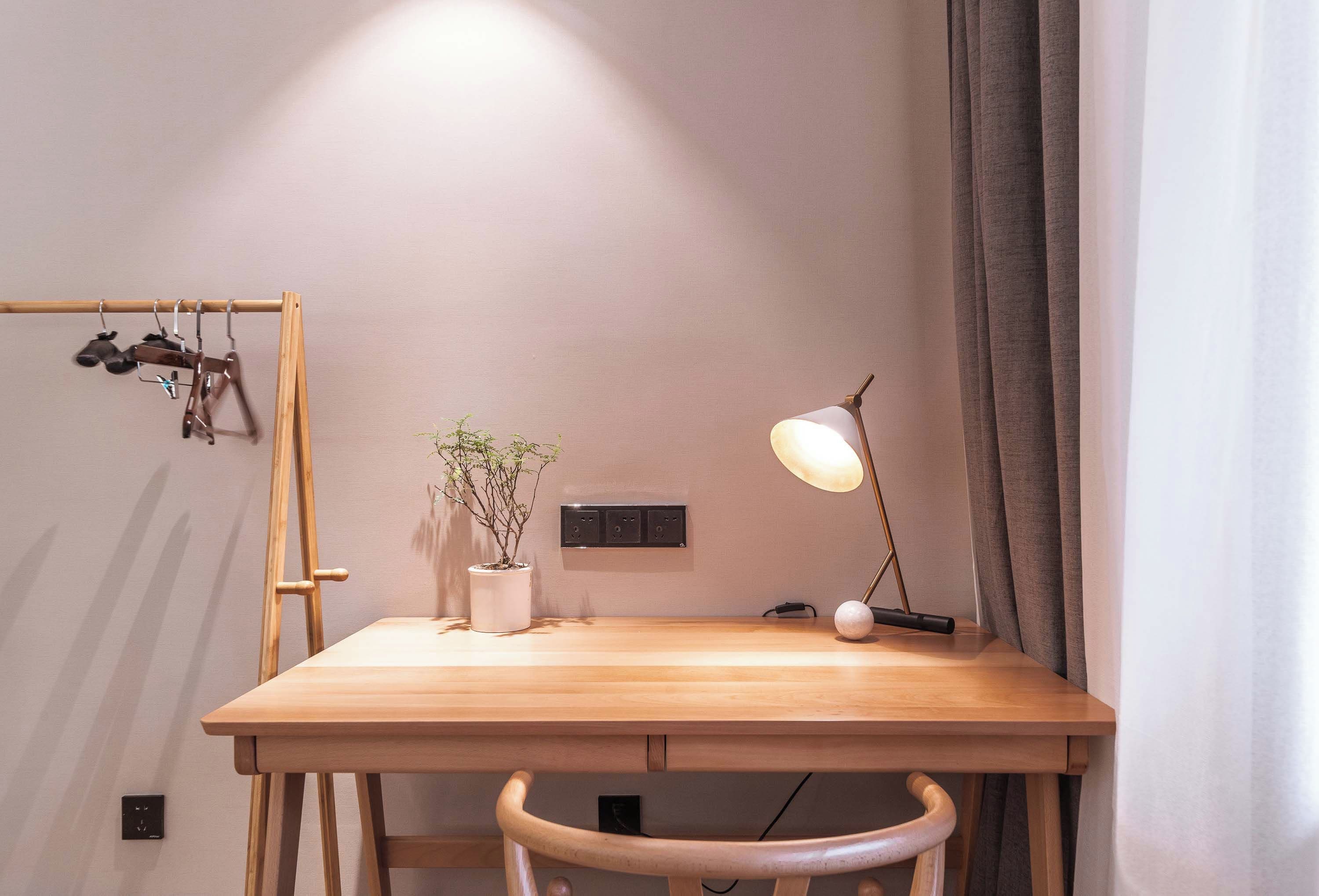 Un bureau en bois, agrémenté d’une plante en pot, d’une lampe de bureau et d’un porte-chaussures suspendu.