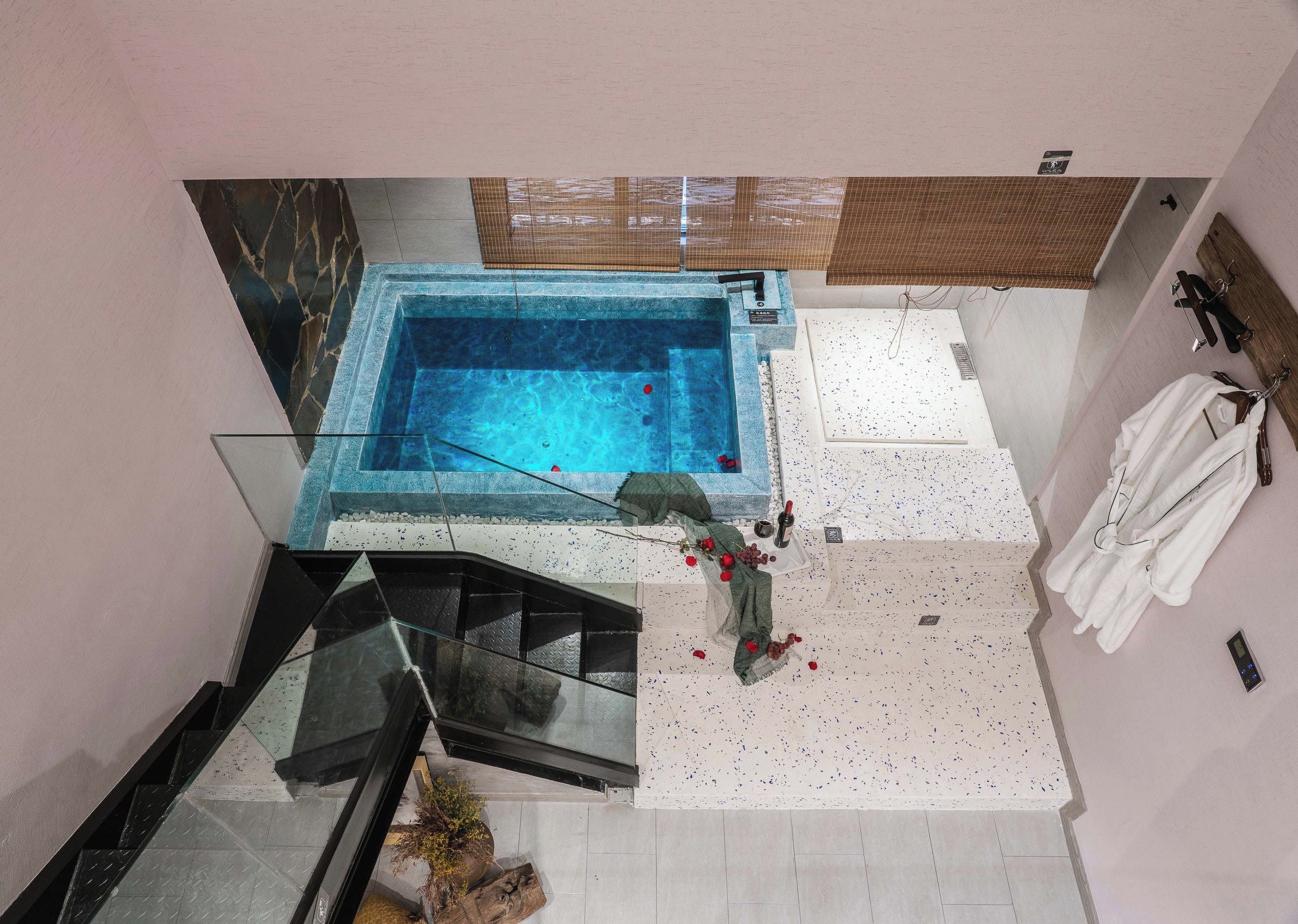 Un baño moderno con bañera de hidromasaje con mampara de vidrio, zona de ducha y escalera que lleva a un nivel superior.