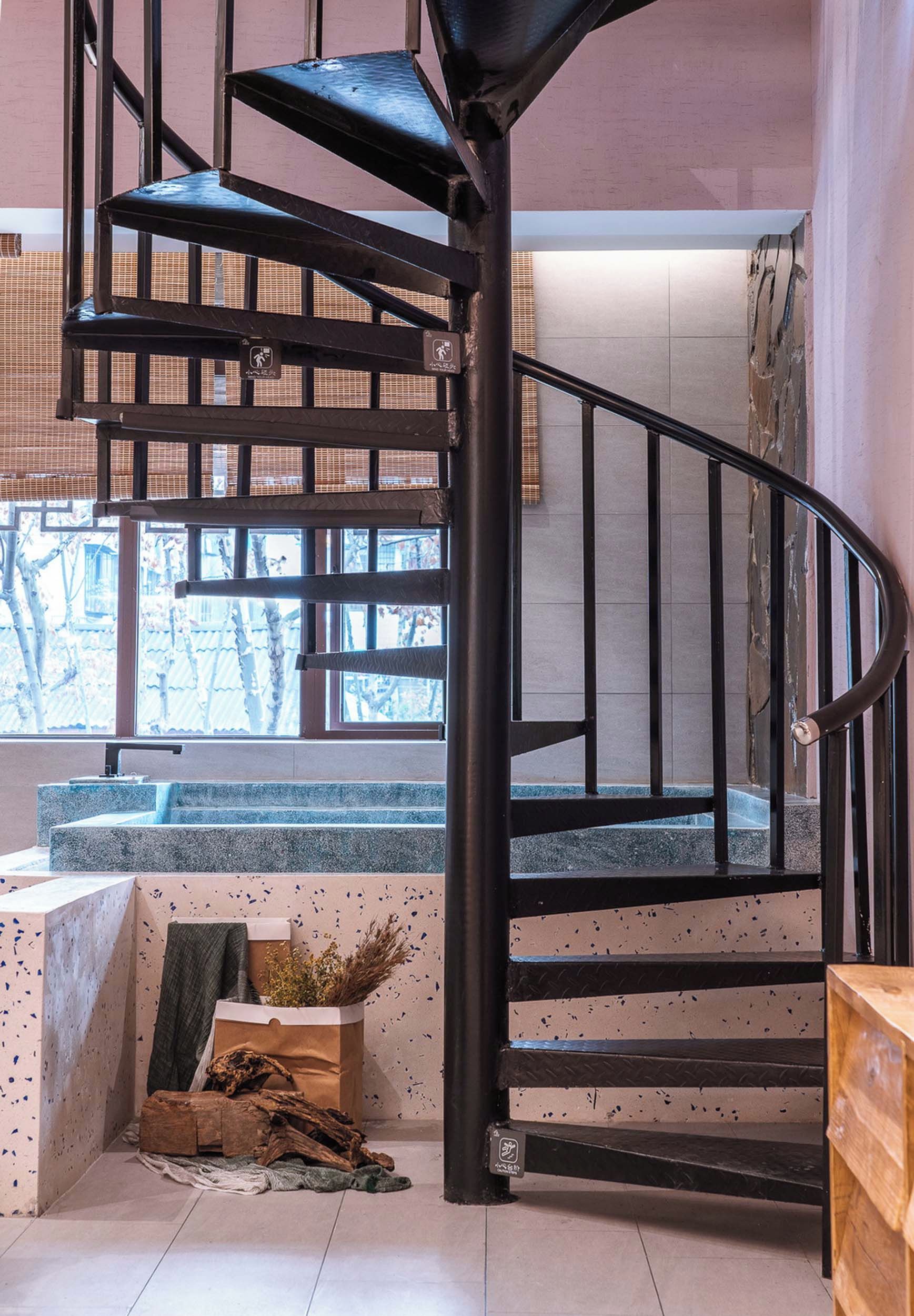 A spiral staircase with a black metal railing and a view of the outside through large windows.