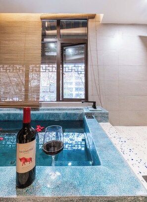 A bottle of Redmore Estate wine and a glass of red wine on a poolside area with a view of a building through a window.