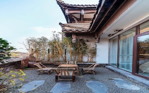 Um edifício tradicional japonês com telhado de telhas, mesa de madeira com cadeiras e um pátio de cascalho.