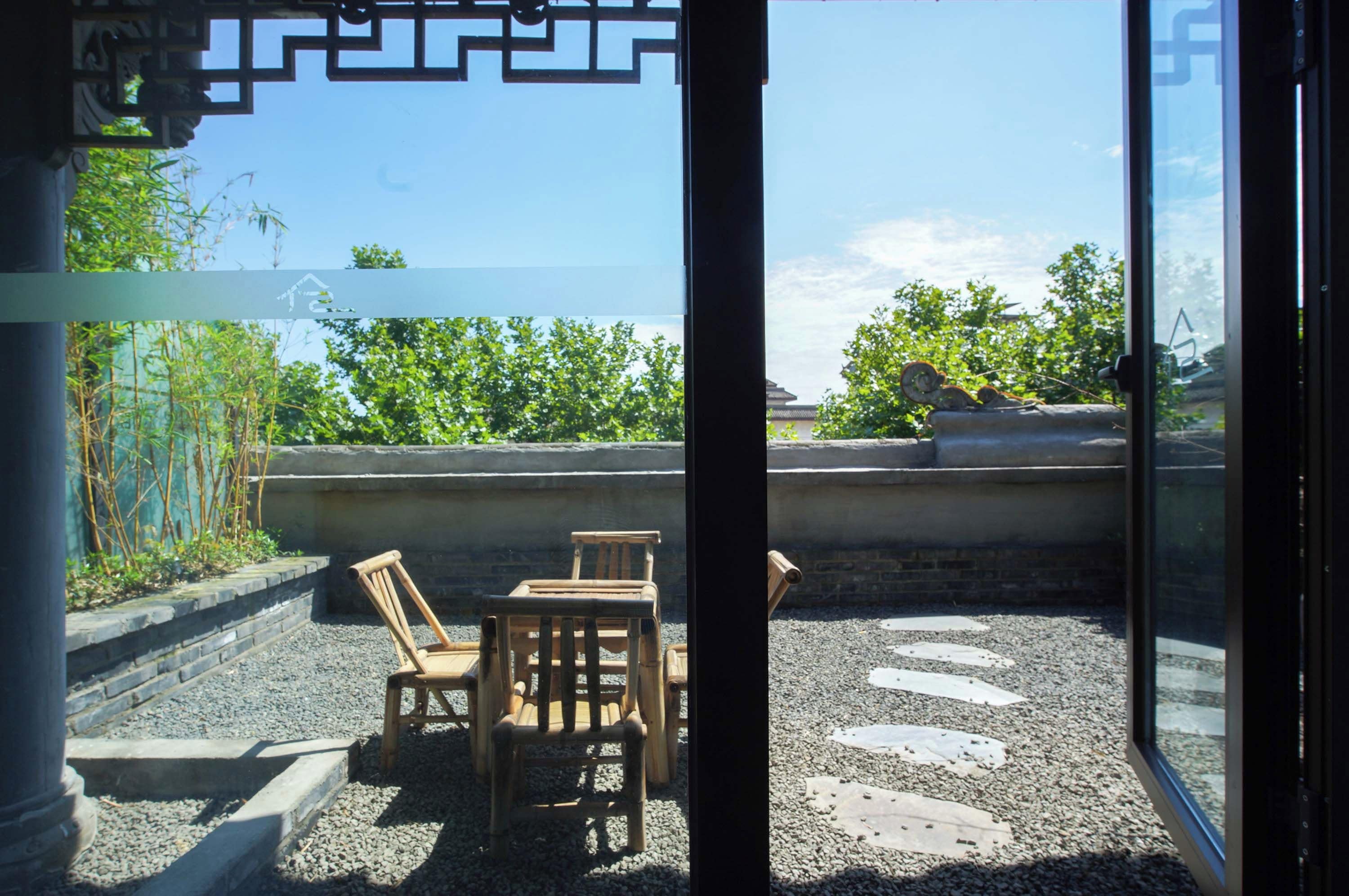 A view from inside a building looking out to a balcony with a table and chairs, a railing, and greenery.