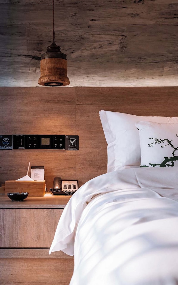 A bedroom with a wooden headboard, a bedside table with a lamp, a clock, and a small decorative item.