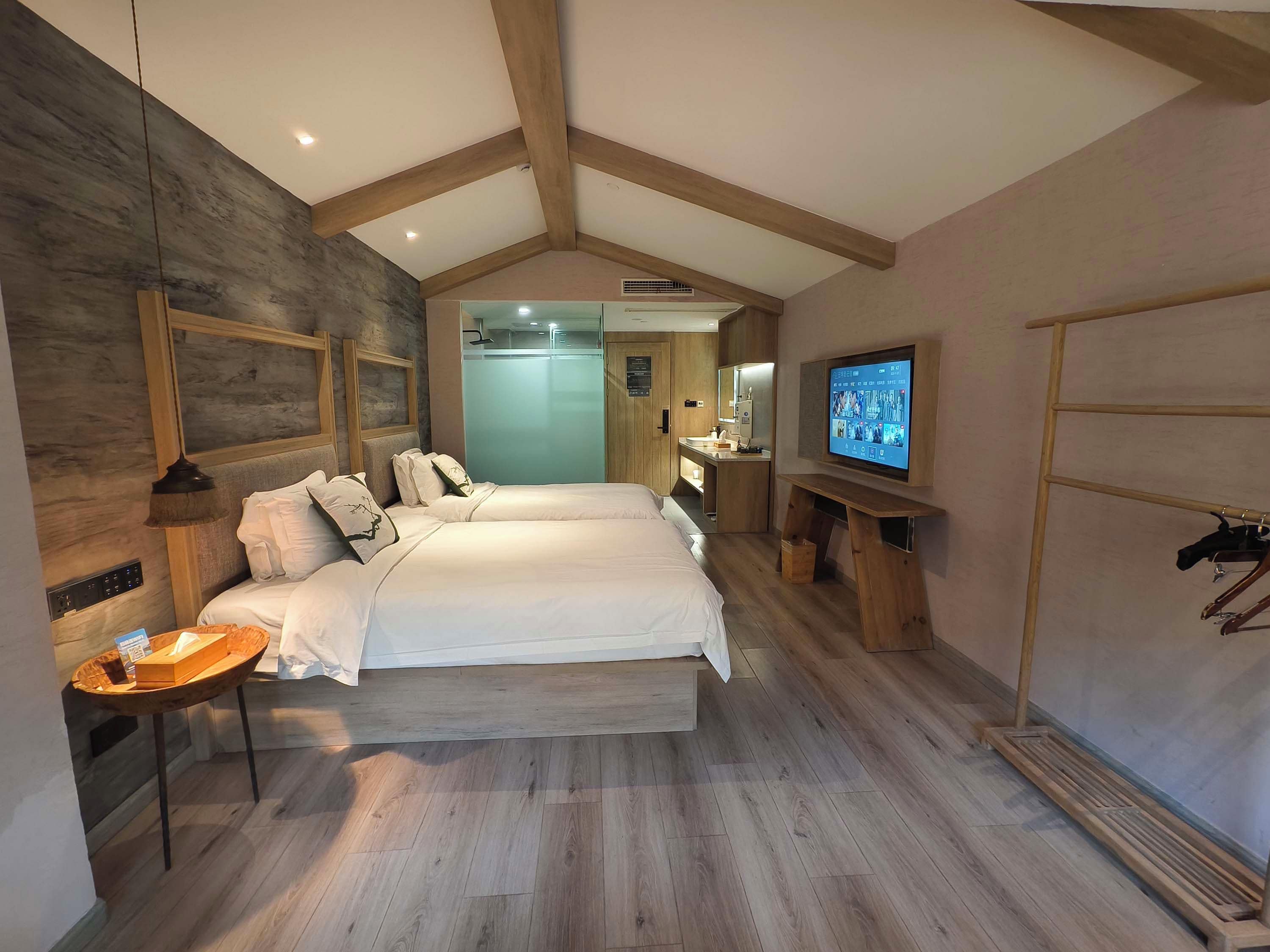 A hotel room with a large bed, a TV, a wooden desk, and a wardrobe.
