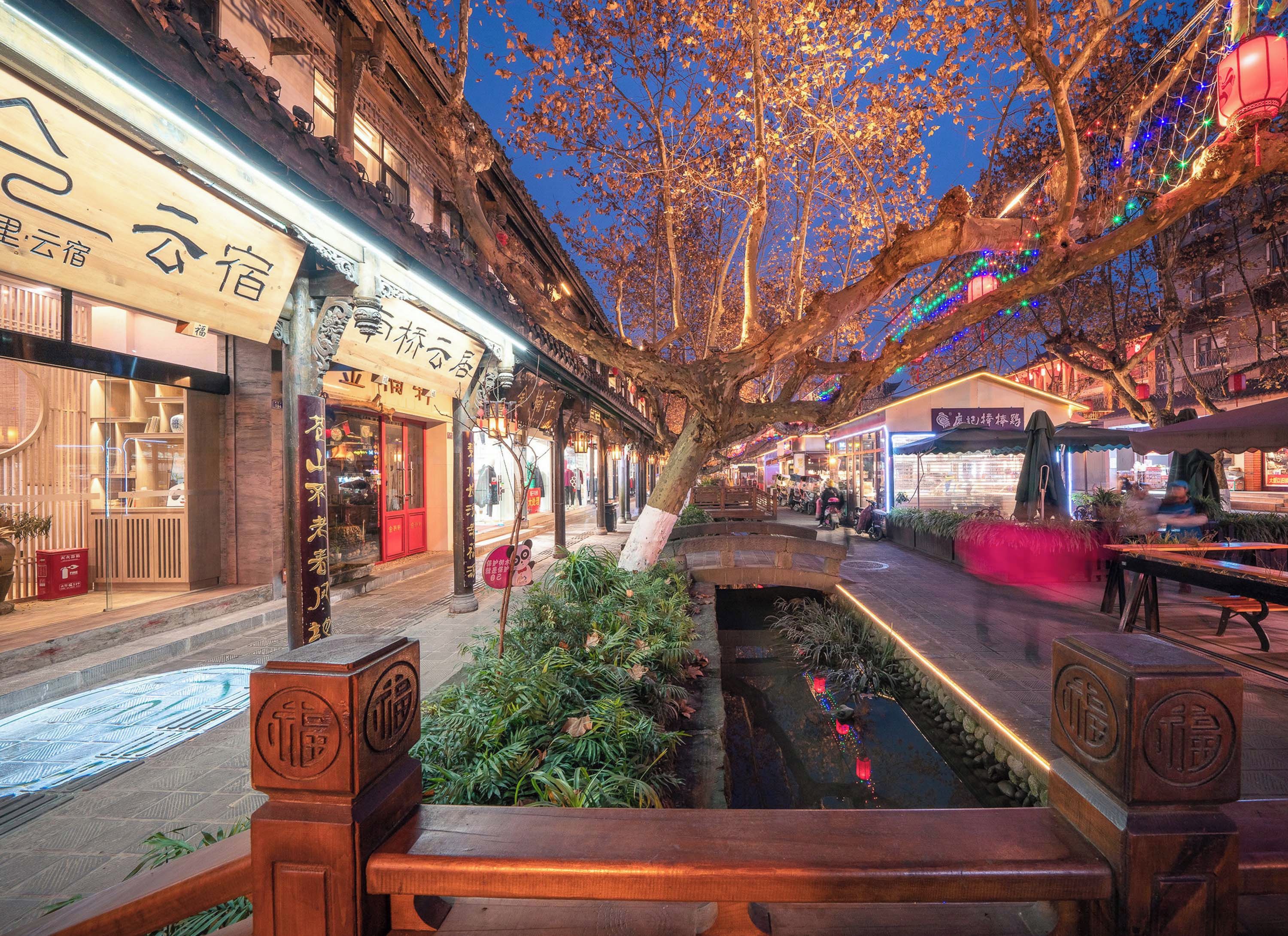 A traditional street with shops, a small water feature, and wooden benches.
