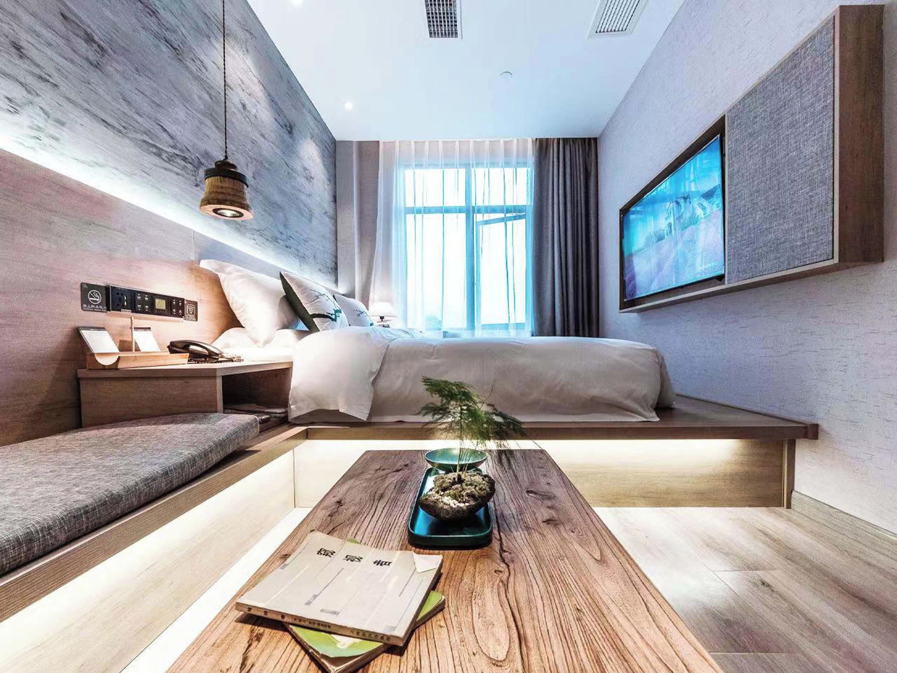 A modern bedroom with a bed, bedside table, and a desk with a plant.