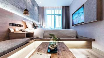 A modern bedroom with a bed, bedside table, and a desk with a plant.
