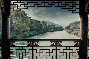 A view through a traditional Chinese window with geometric patterns, overlooking a river flanked by lush greenery and distant hills. - Yunfuli Yunsu·Dujiangyan Nanqiao Yunju (Dujiangyan Scenic Area Nanqiao Branch) (Chengdu)