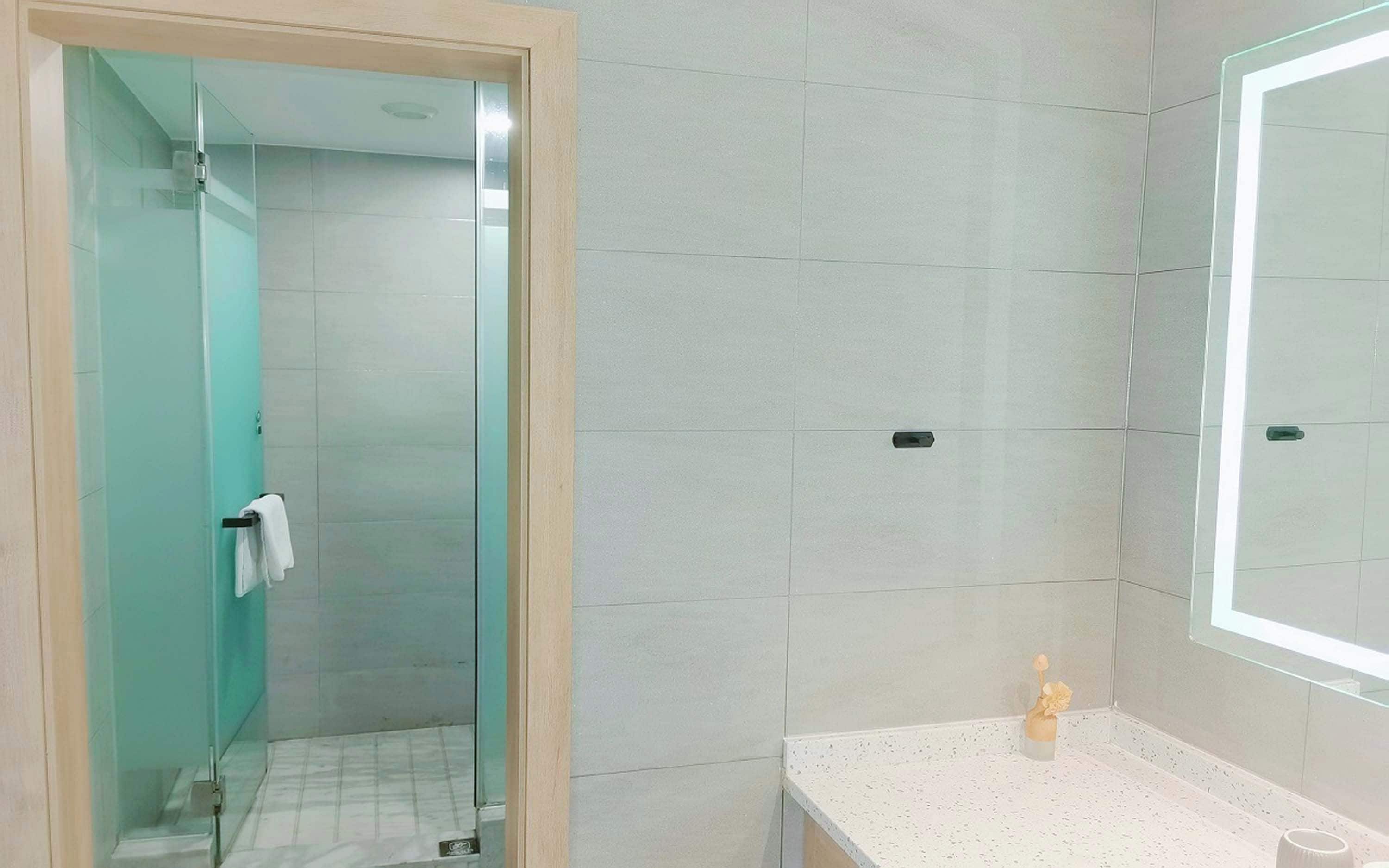 A bathroom with a glass shower enclosure, a white sink with a vase of flowers, and a mirror.