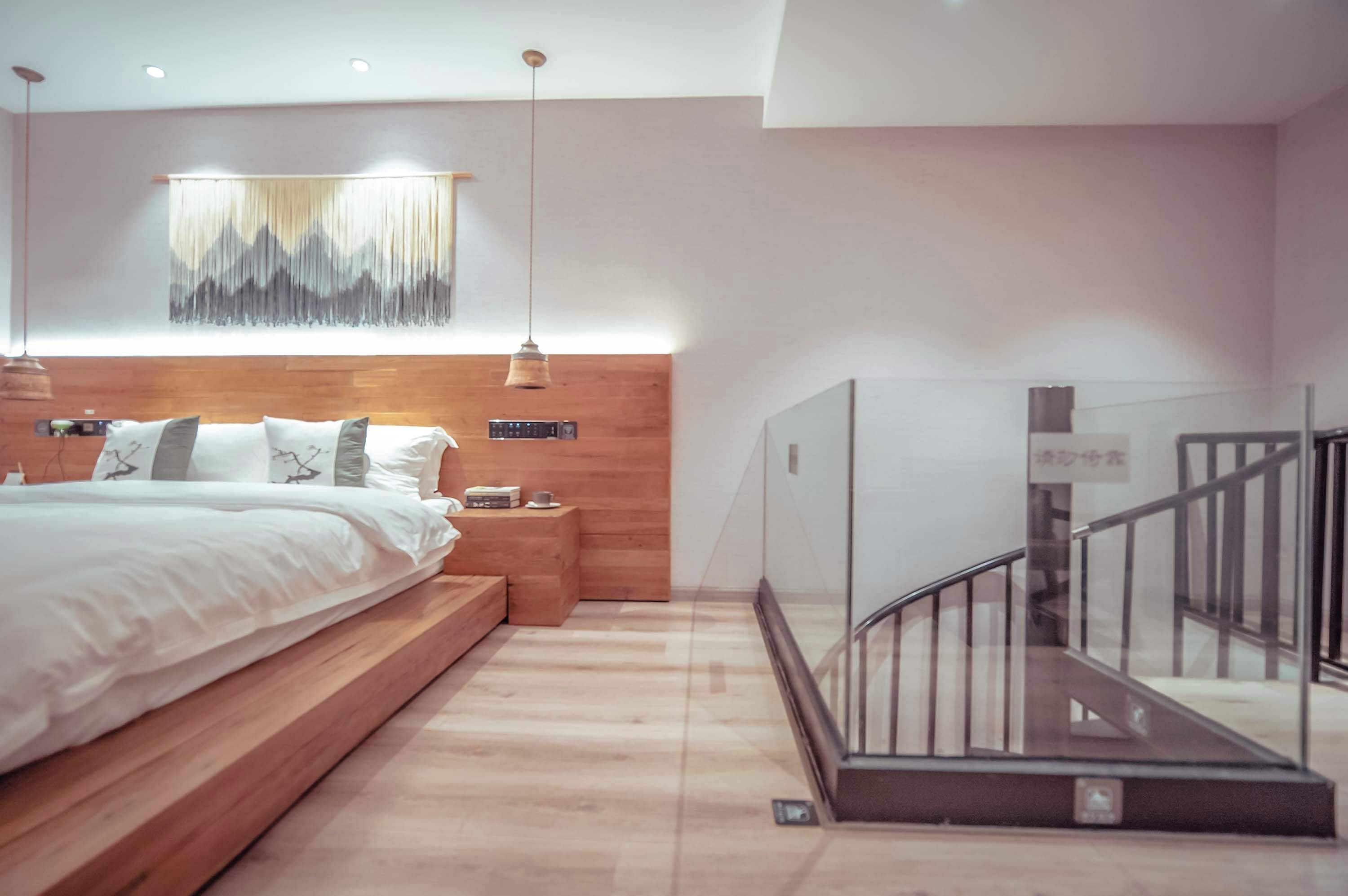 A modern bedroom with a wooden bed, bedside tables, a mounted TV, and a staircase with glass railings.