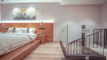 A modern bedroom with a wooden bed, bedside tables, a mounted TV, and a staircase with glass railings.
