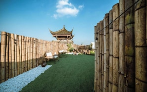 A courtyard with a traditional pavilion, bamboo walls, and a seating area with a hanging chair.
