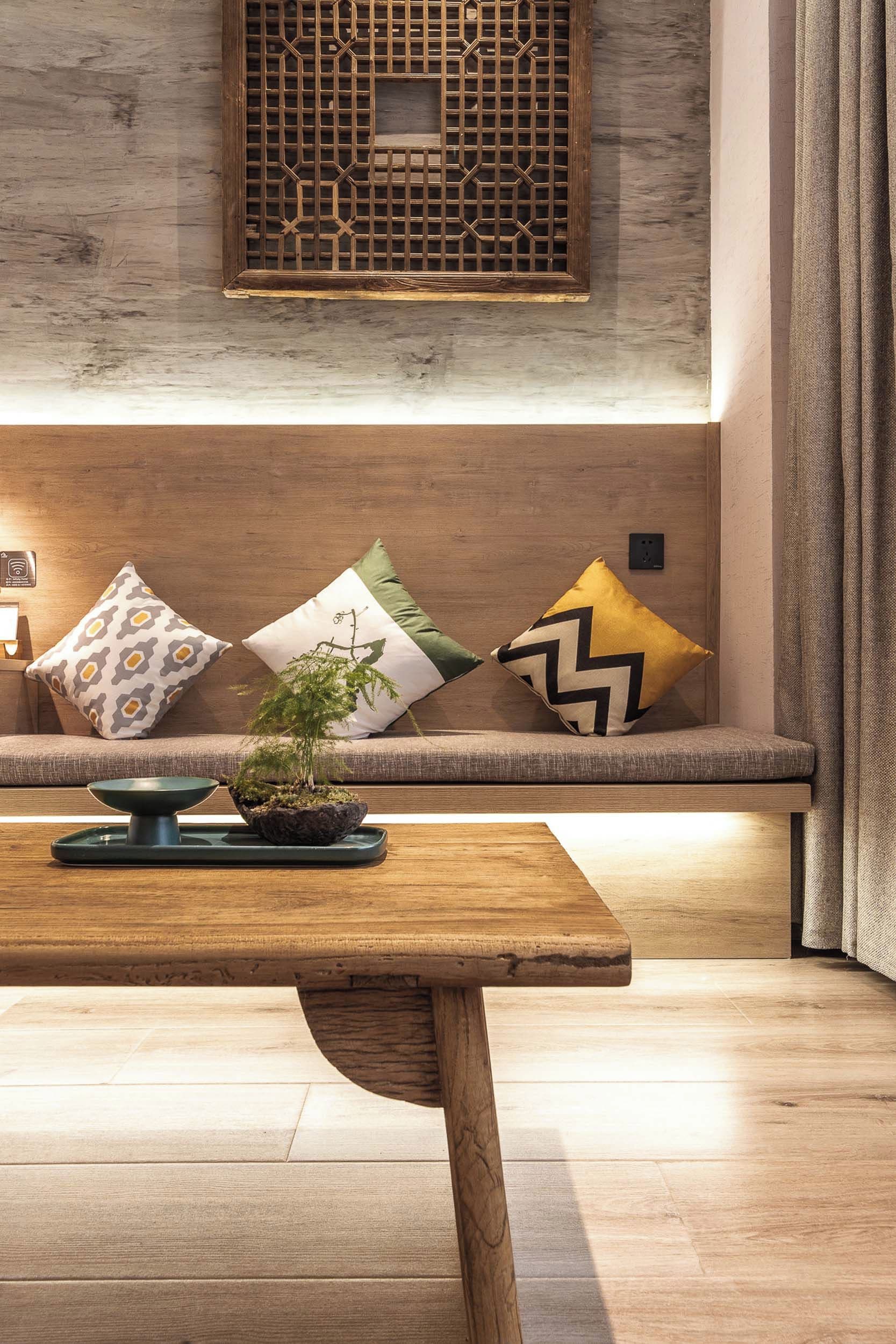 Una sala de estar moderna con un banco de madera, una mesita con una planta y cojines decorativos.
