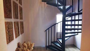 A staircase with a black railing leading to an upper floor, a wooden floor, and a wall with multiple framed artworks.
