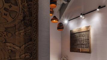 Une pièce agrémentée d’un panneau décoratif en bois, d’un luminaire suspendu, d’une applique murale et d’une petite étagère sur laquelle sont disposés des objets décoratifs.