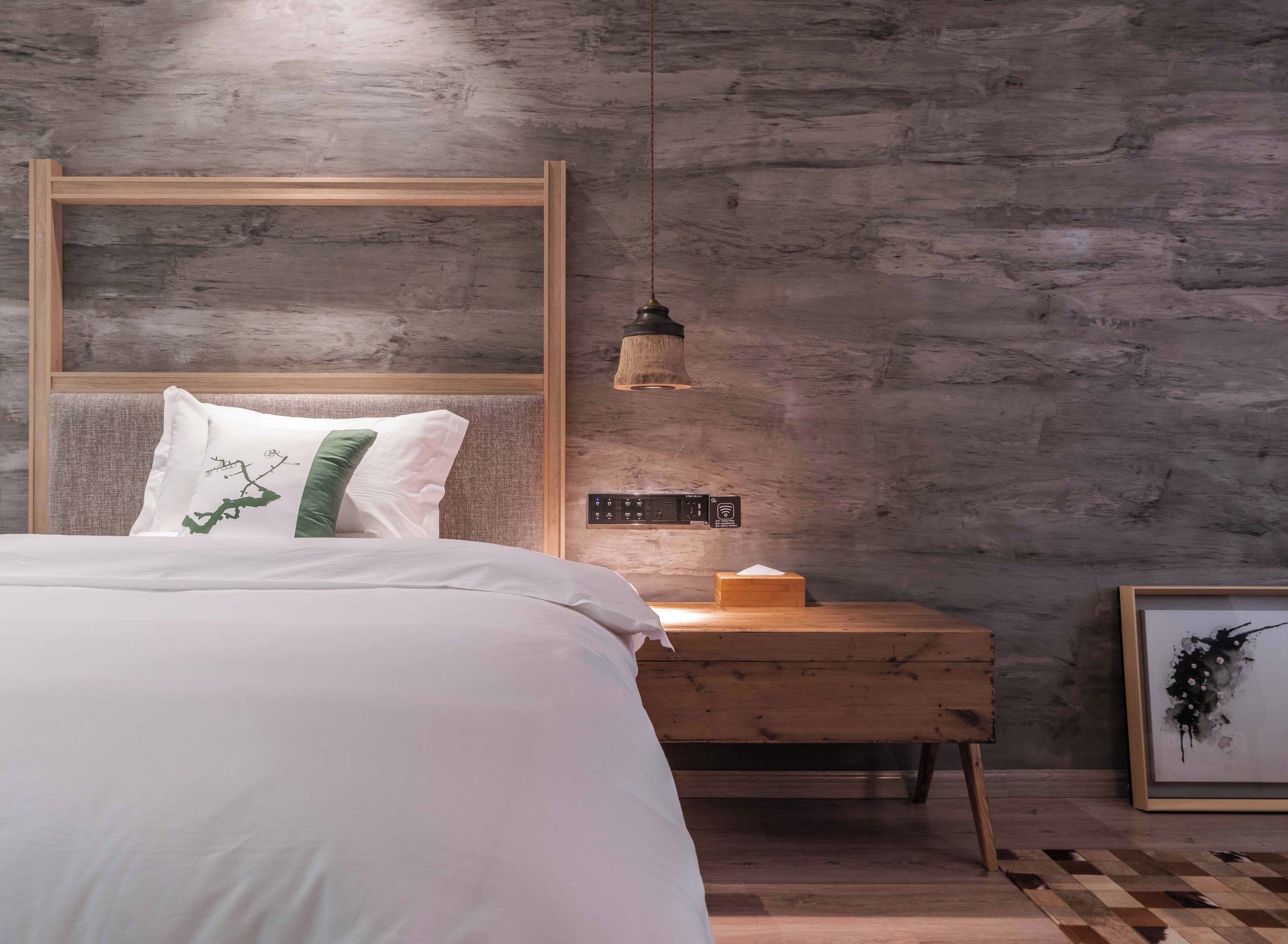 Un dormitorio con una cama, una mesita de noche, una lámpara y una obra de arte enmarcada.