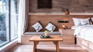 A modern bedroom with a wooden headboard, a bedside table with a lamp, and a view of greenery outside.