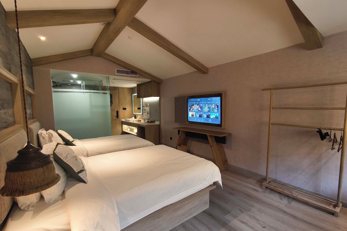 Quarto de hotel com duas camas, uma televisão presa a um suporte de madeira, um espelho e um guarda-roupa de madeira.