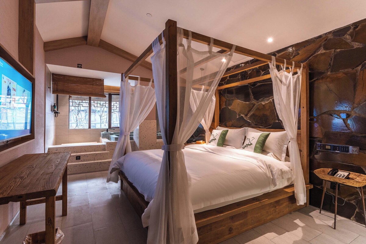 Quarto com uma cama de dossel, parede de pedra, mesa de madeira e televisão.