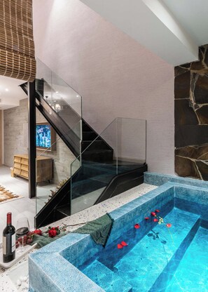 A modern interior with a glass staircase leading to a living area, a stone wall, and a pool with floating flowers.