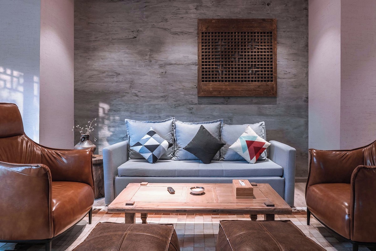 Uma área de estar moderna com sofá azul, poltronas de couro, mesa de centro de madeira e um painel decorativo na parede.