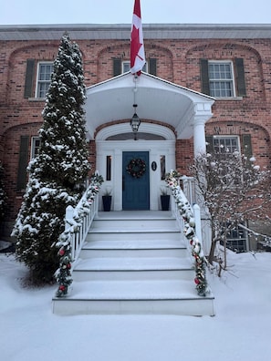Een bakstenen gebouw met een besneeuwde ingang, een Canadese vlag en een krans bij de deur.