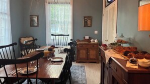 Een eetkamer met een houten tafel voor vier personen, omringd door stoelen, een kroonluchter en een raam met dunne gordijnen.
