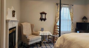 A hotel room with a bed, a chair, a small table, a television, and a fireplace.