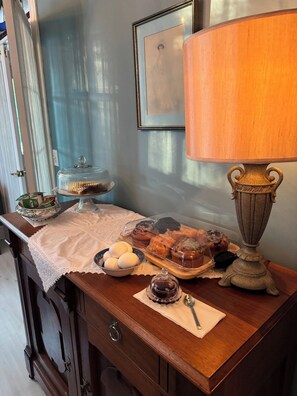 Una mesa de madera con mantel de encaje, una lámpara, un cuenco de huevos, una bandeja de pasteles y una lámpara de estilo vintage.