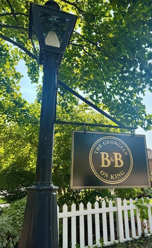 Eine Straßenlaterne mit einem Schild für 'The Georgian B&B on King' vor einem weißen Zaun aus Holzlatten.