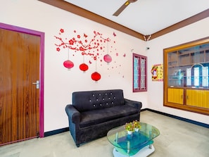 A room with a wooden door, a dark sofa, a glass coffee table with flowers, and a wall with red decorations. - Premium Ganapathy Athipalayam Pirivu (Coimbatore)