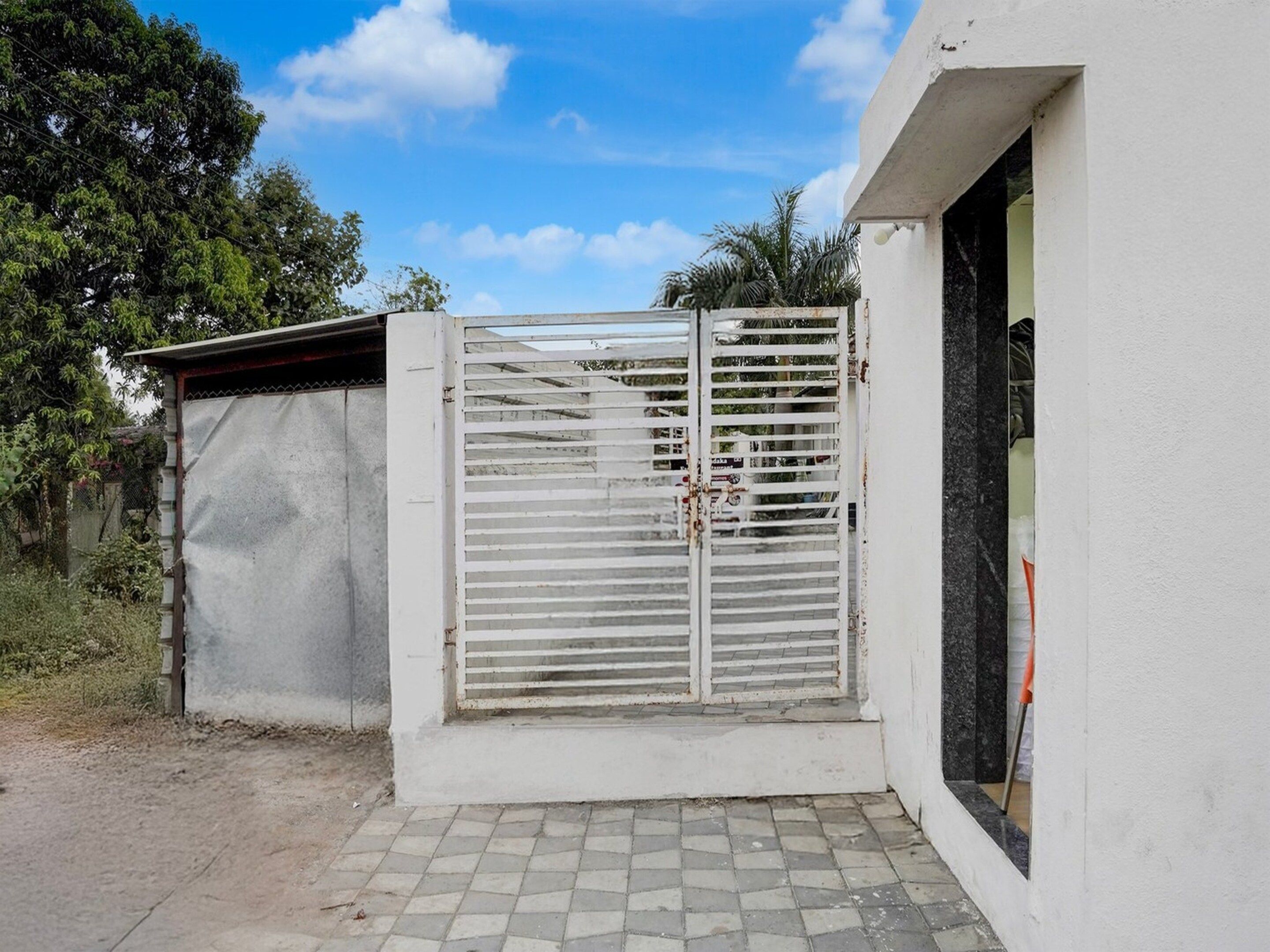A gated entrance with a metal gate, a concrete wall, and a tiled ground.