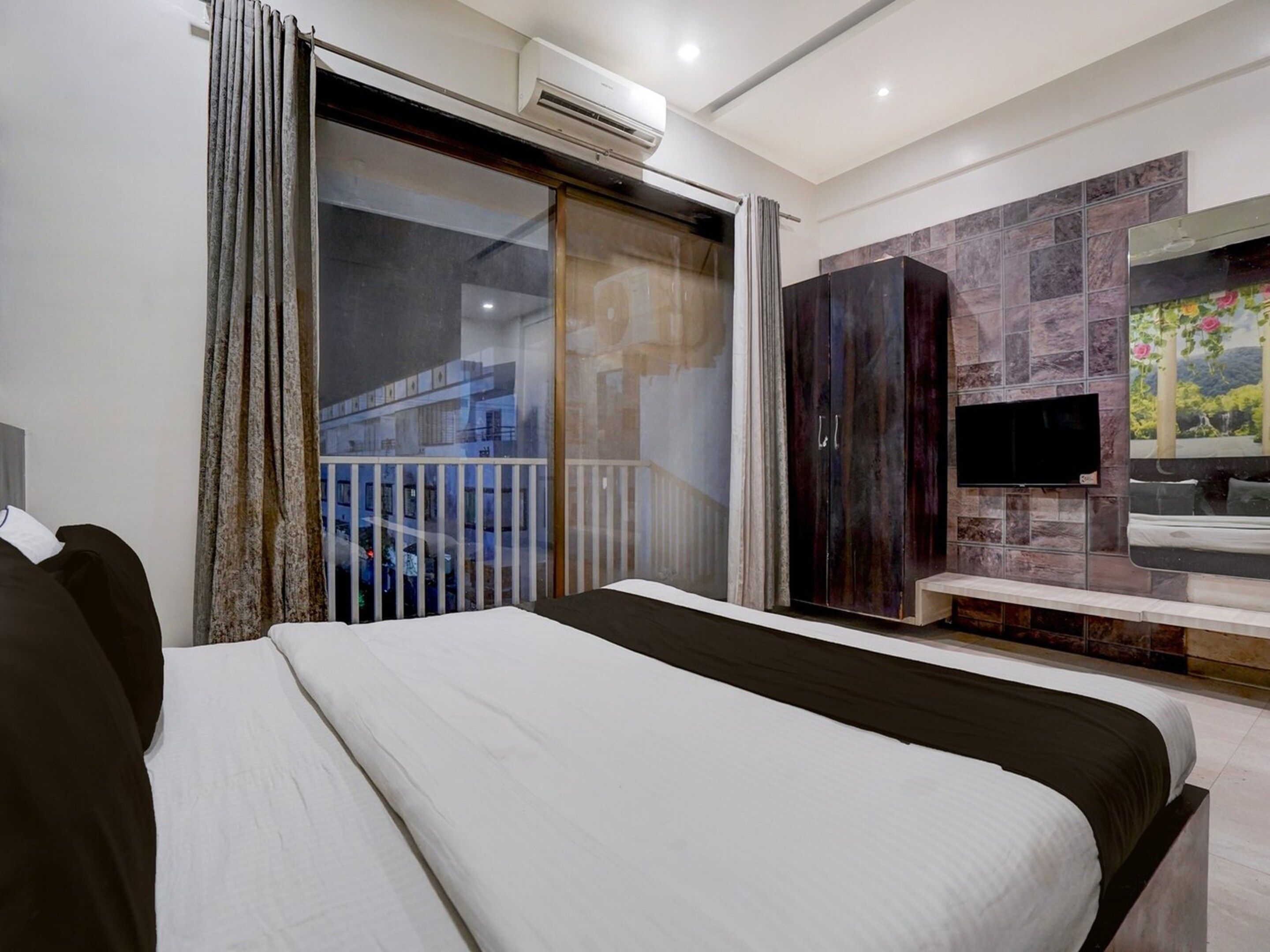 A hotel room with a bed, a television, a bathroom with a mirror, and a balcony with curtains.