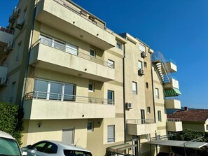 Un immeuble à plusieurs étages, doté de balcons, d’un escalier et d’une voiture garée devant.