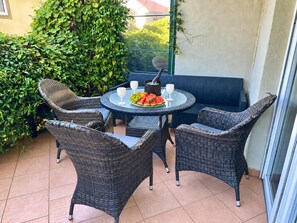 Une table ronde entourée de chaises en osier, une bouteille de champagne et une assiette de fruits.