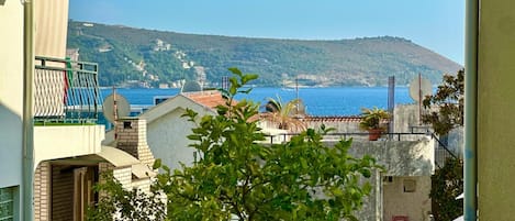 A coastal residential area with buildings, a view of the sea, and a hill in the background.