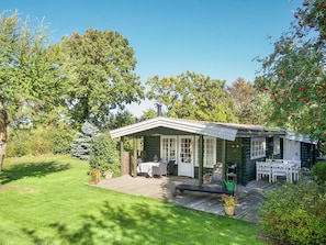 A log cabin with a porch, a table, and chairs, surrounded by a well-maintained lawn and trees. - 6 Person Holiday Home in Hundested (Hundested)