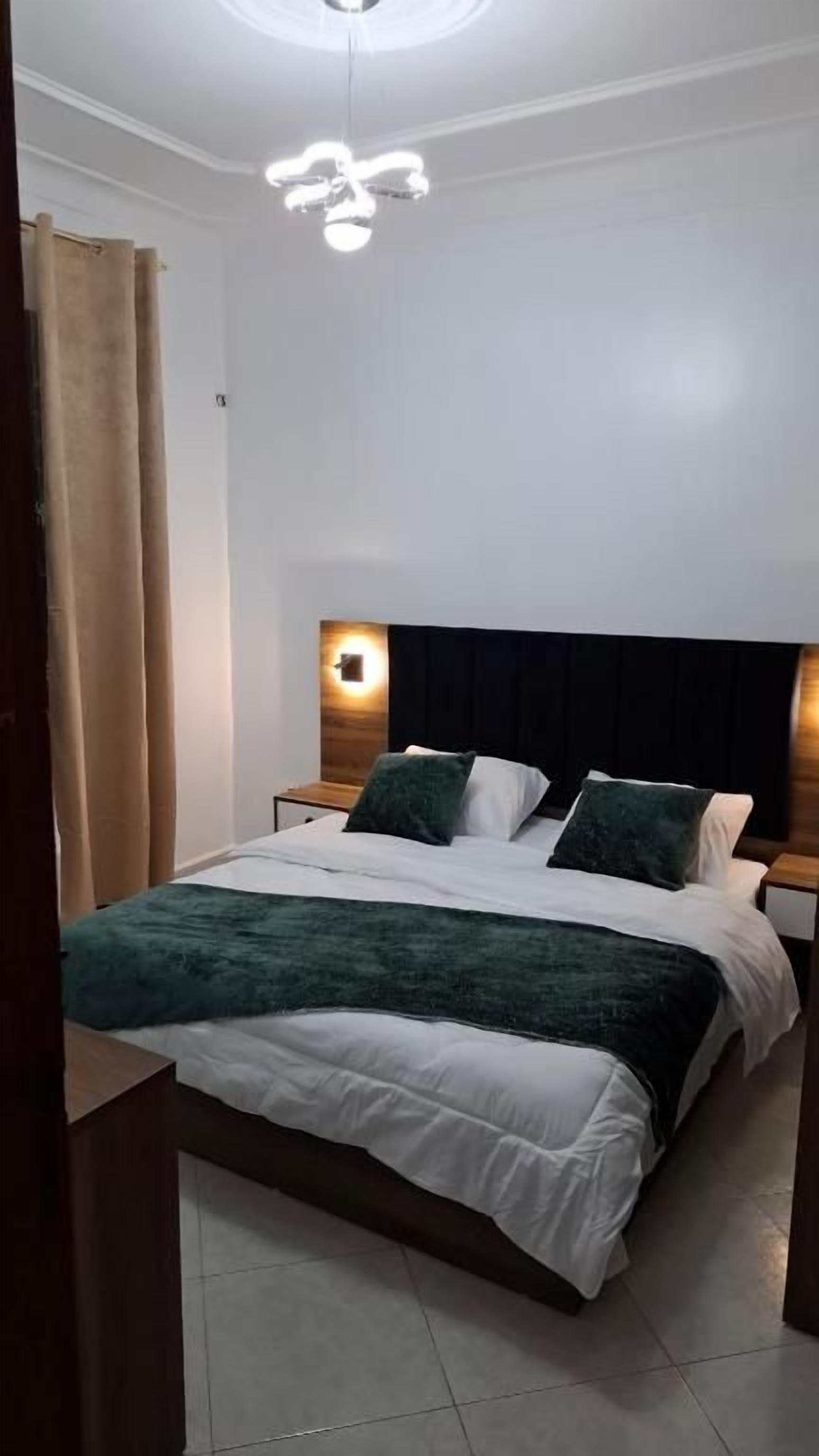 Un dormitorio con cama, mesitas de noche, cabecera y lámpara de techo.